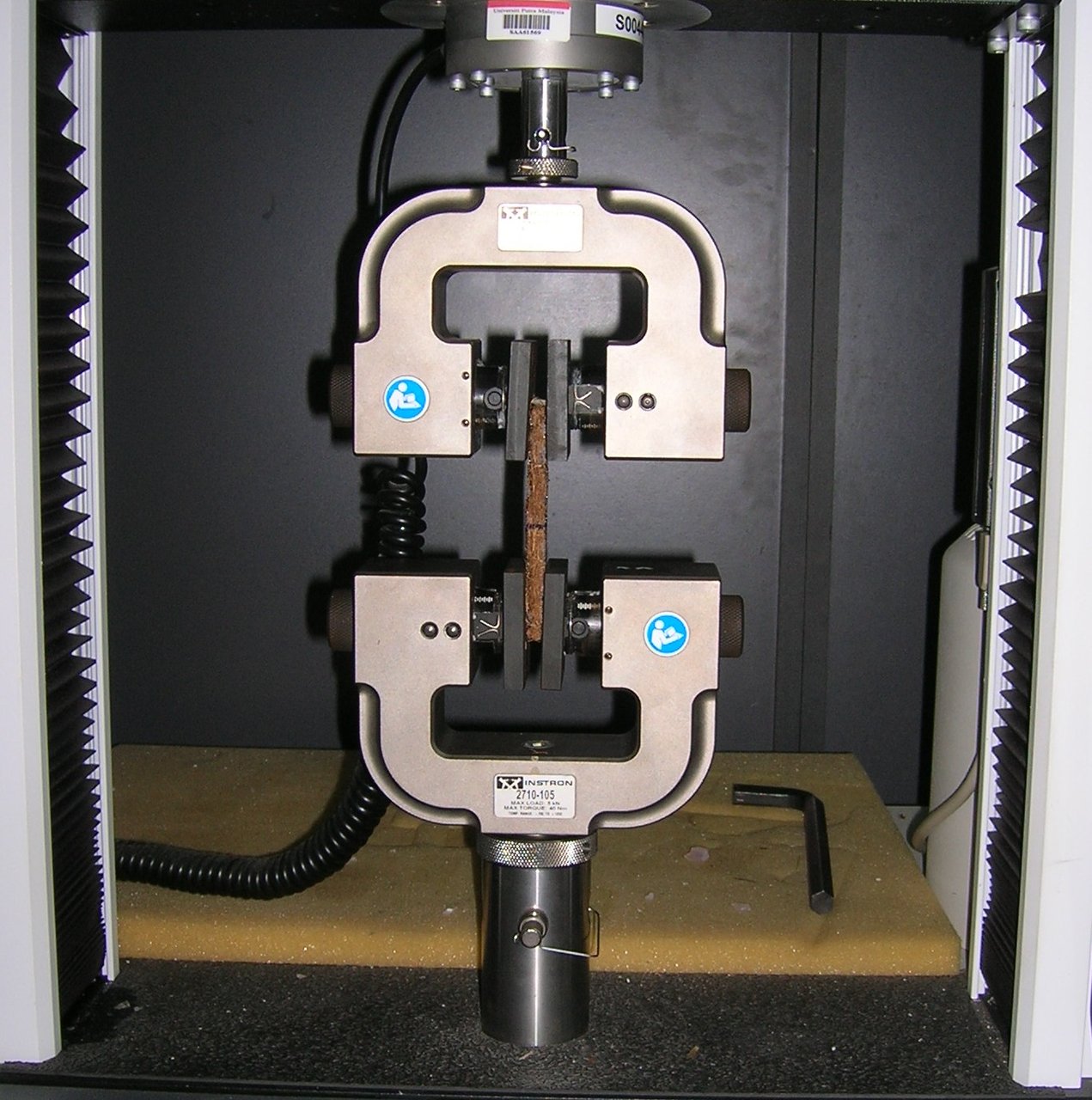 Máquina de ensaio de tração com um corpo de prova metálico preso entre duas garras.