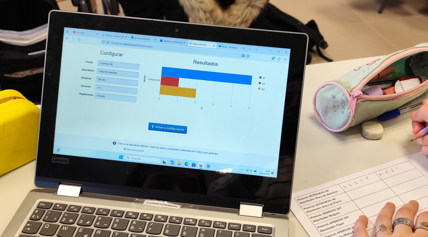 Estudiante observando en un ordenador los resultados del laboratorio remoto de radiactividad y anotando datos.
