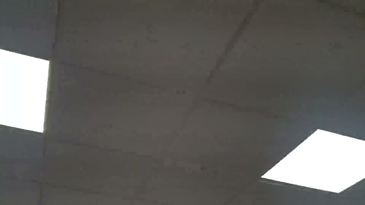 Uma imagem comum de placas de forro, com uma luminária retangular brilhante à esquerda e outra na parte inferior direita. Pequenas marcas aparecem de forma discreta entre elas.